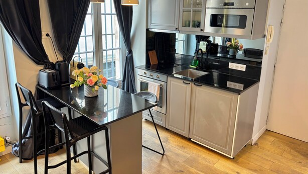 A modern kitchen with a central island, stainless steel appliances, and a view through the window. - Odéon Saint Germain - Central Flat Aldaro (Paris)