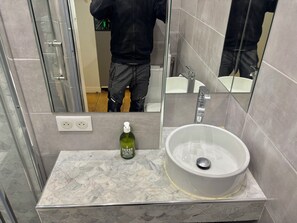 Ein Badezimmer mit Marmorplatte, einem weißen Waschbecken, einem Spiegel und einer grünen Handseifenflasche.