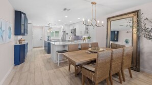 A modern kitchen with white cabinets, a central island, and a dining area with wicker chairs.