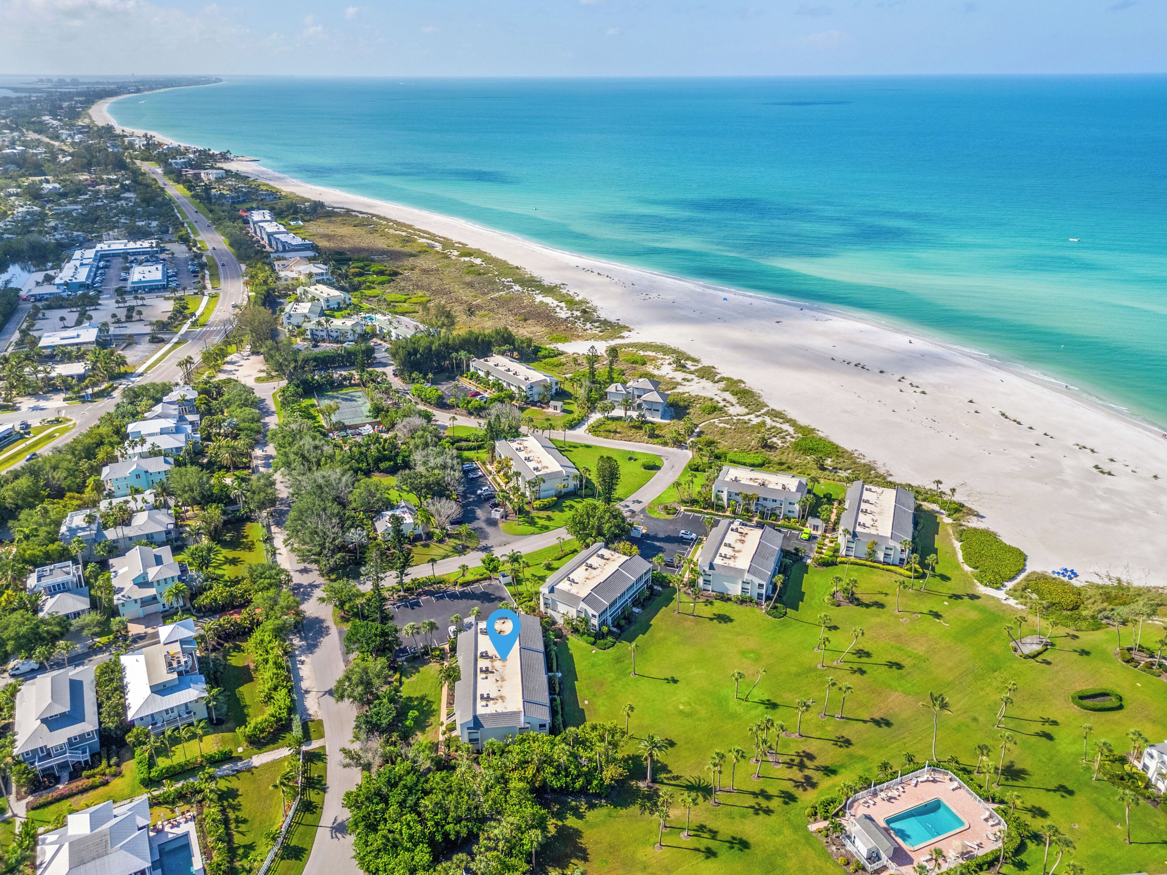 An aerial view of a coastal resort with multiple buildings, a beach, and a swimming pool.