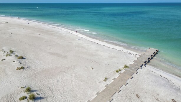 A beach with a clear view of the ocean, a sandy shoreline, and a concrete walkway along the water's edge.