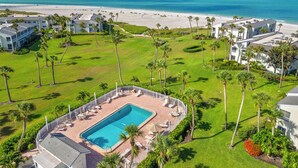 A resort with a swimming pool, beach view, and palm trees.
