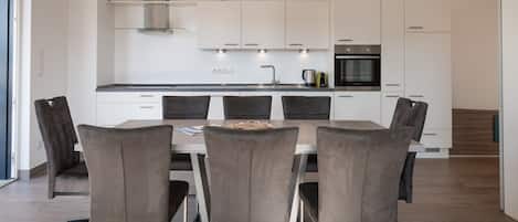 A modern kitchen with white cabinets, a stainless steel range hood, and a built-in oven.