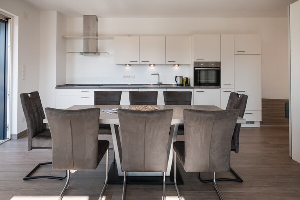 A modern kitchen with white cabinets, a stainless steel range hood, and a built-in oven.