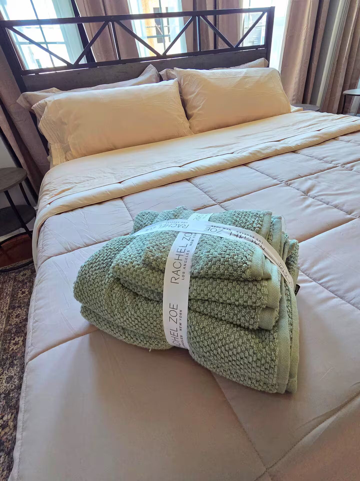 A neatly made bed with a quilted headboard, a folded green blanket, and a pillow.