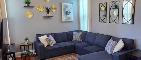 A living room with a sectional sofa, a patterned rug, decorative wall art, and a modern chandelier.