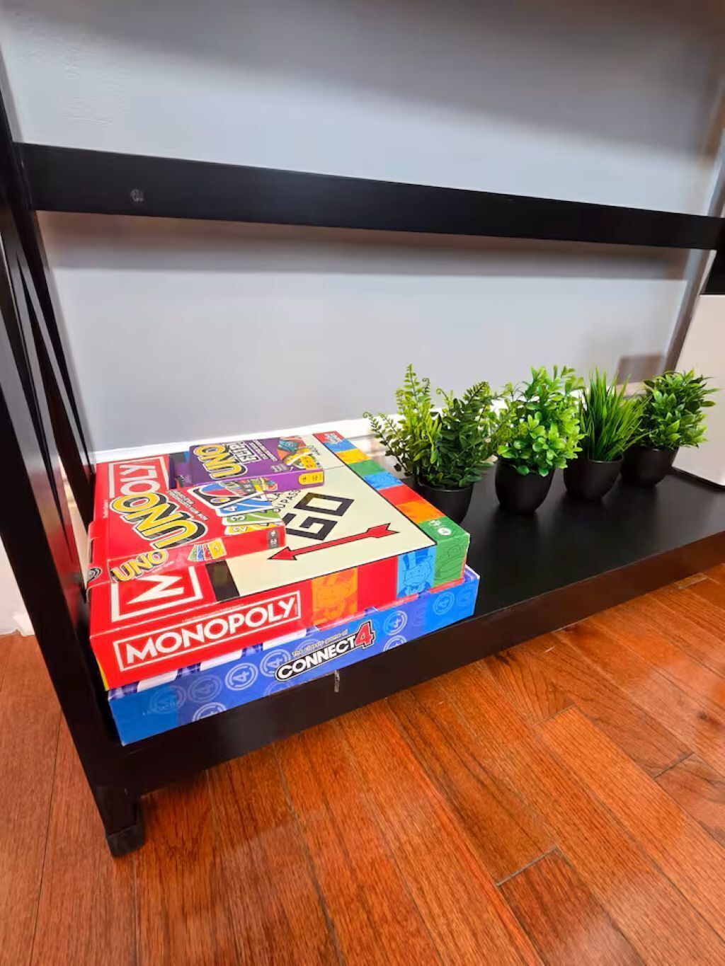 A wooden shelf with a Monopoly game box and four potted plants.