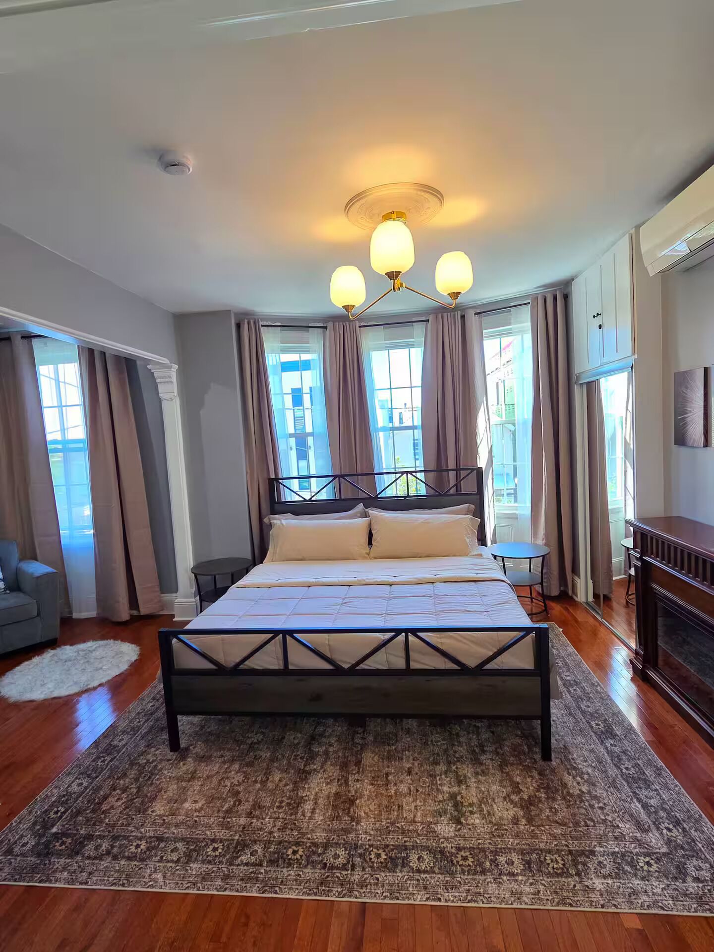 Un dormitorio con una cama grande, una araña, un escritorio y vistas a través de las ventanas.
