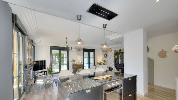 Una cocina moderna con una isla central, iluminación colgante y un horno empotrado.
