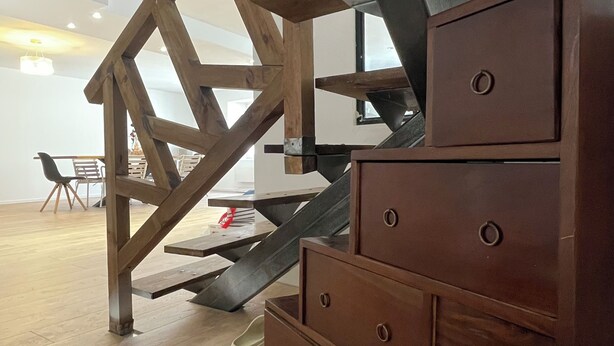 A staircase with wooden beams, a brown chest of drawers, and a dining area with chairs and a table. - Spacious, newly renovated townhouse (Toul)