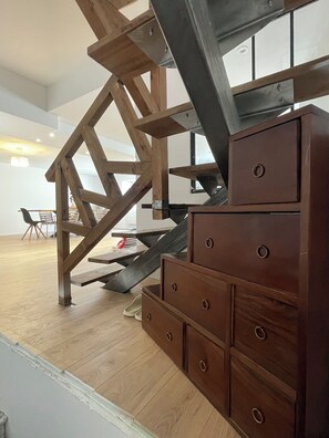 Una escalera con vigas de madera, un aparador marrón y un comedor con sillas y una mesa.