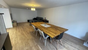 A spacious room with a wooden dining table, modern chairs, a sofa, and a ceiling light fixture. - Spacious, newly renovated townhouse (Toul)