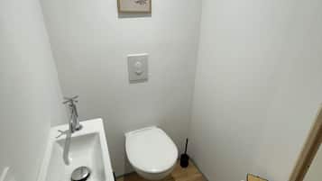 Un baño pequeño y blanco con suelo de madera, un lavabo blanco, un inodoro y un cuadro en la pared.