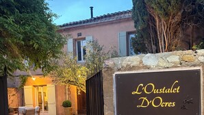 Señal de 'L'Oustalet D'Ocres' con un camino de grava que lleva a un edificio con terraza.