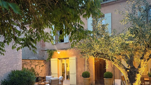 Un patio con piscina, mobiliario exterior y un edificio con puerta y ventanas.