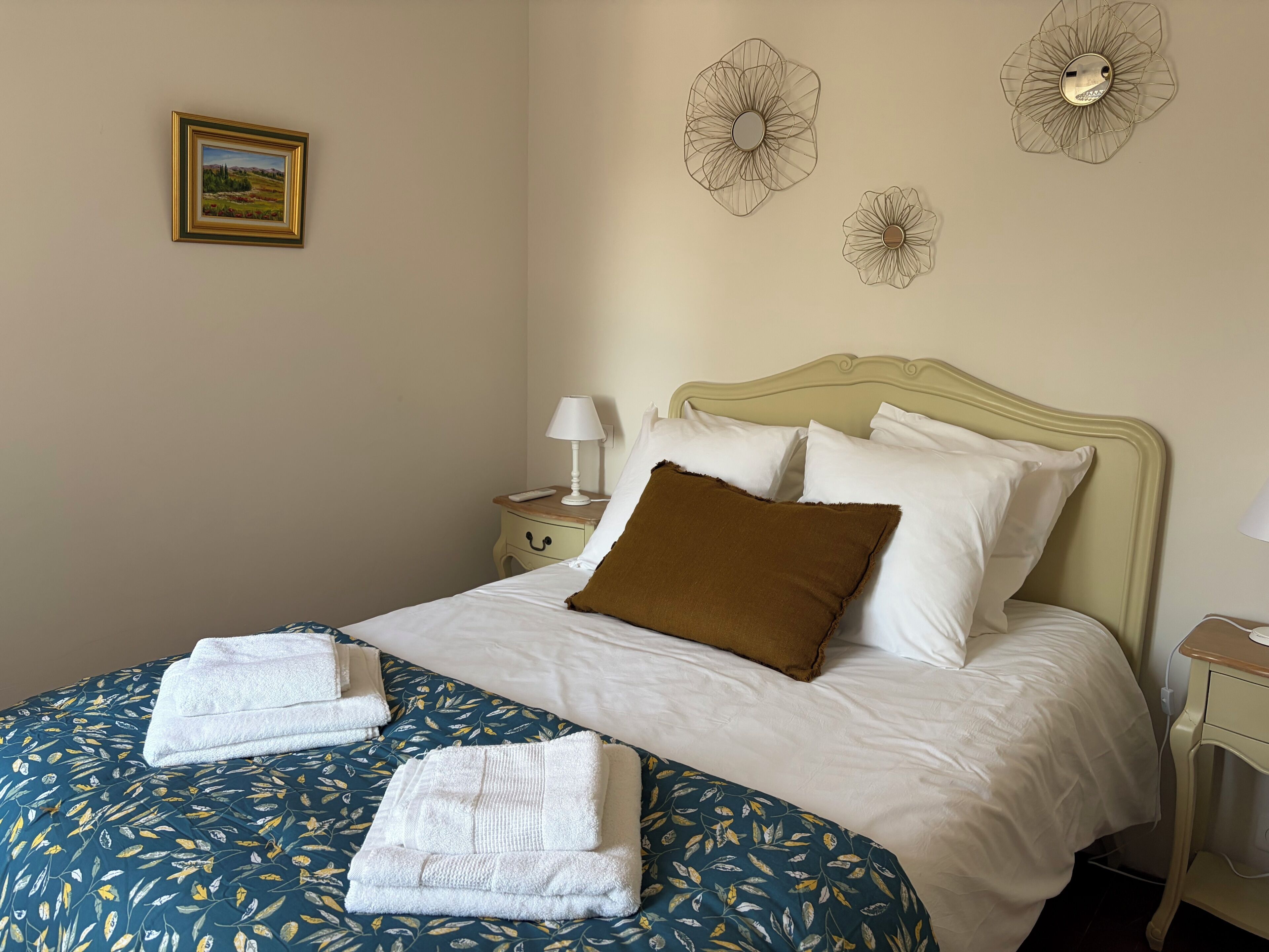 A neatly made bed with white and brown pillows, a blue floral bedspread, and two folded towels.