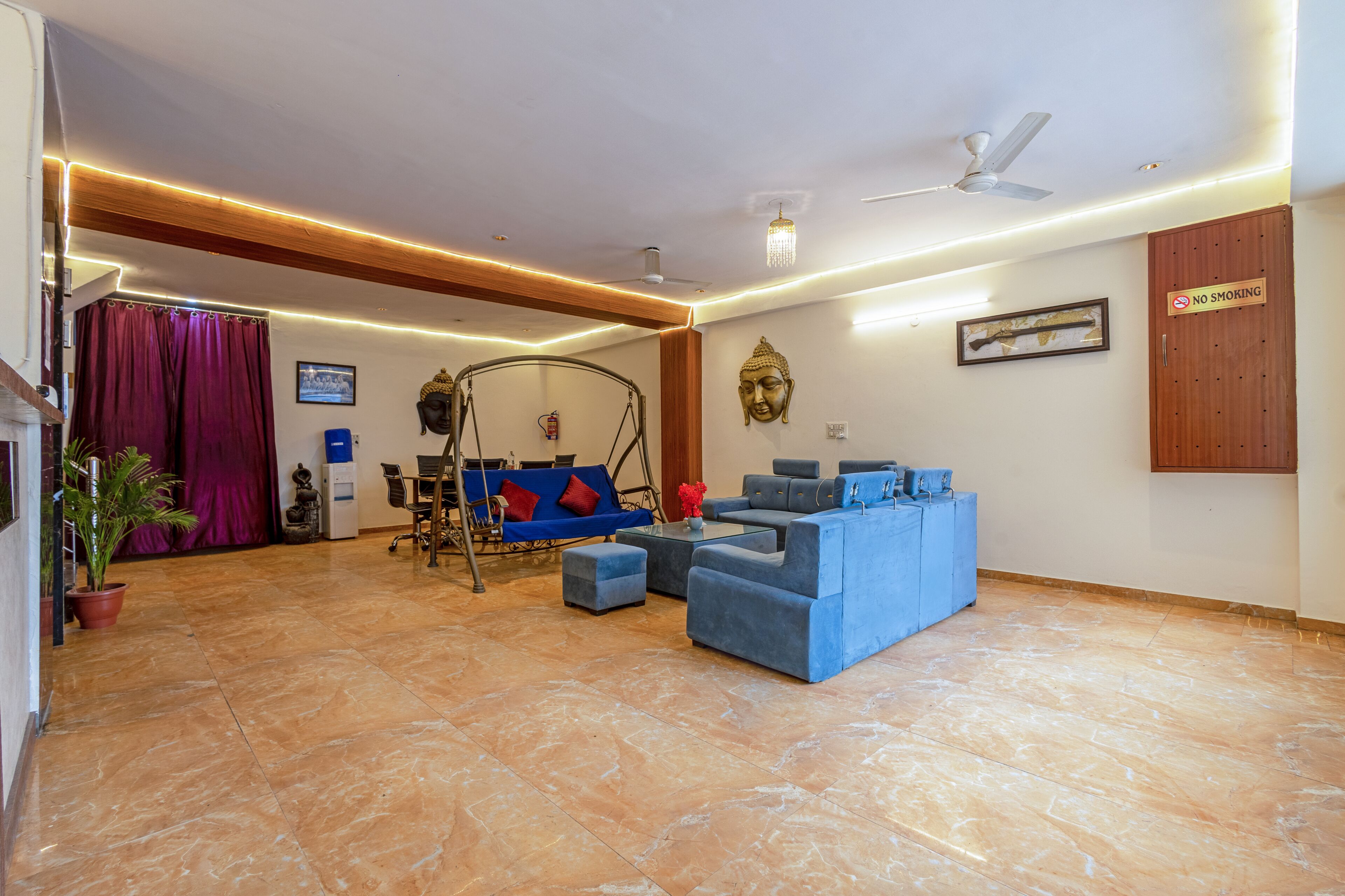 A spacious living area with a blue sofa set, a swing chair, and a dining table with chairs.