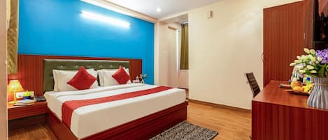 A hotel room with a bed, bedside table, lamp, and a desk with a chair.
