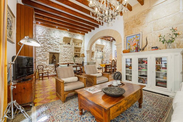 A cozy living room with a stone wall, wooden furniture, a chandelier, and a cabinet with books. - Casa Angels with private pool in the historic center of Pollença (Pollensa)
