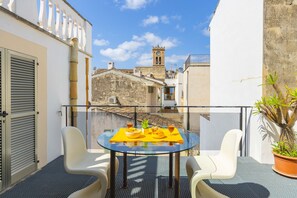 Un balcón con una mesa de vidrio, dos sillas, una planta en maceta y vistas a edificios y una torre.