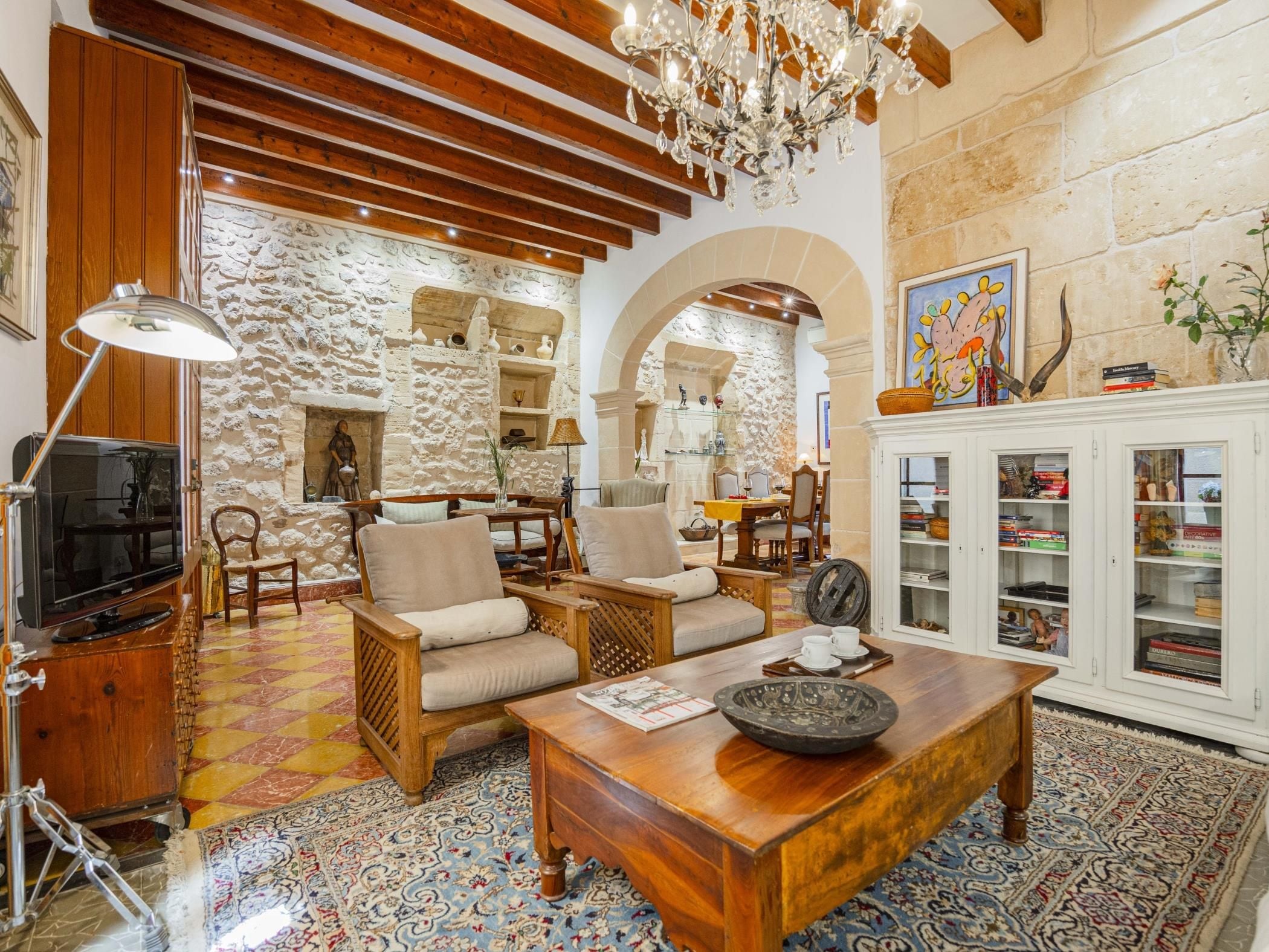 A cozy living room with a stone wall, wooden furniture, and a chandelier.