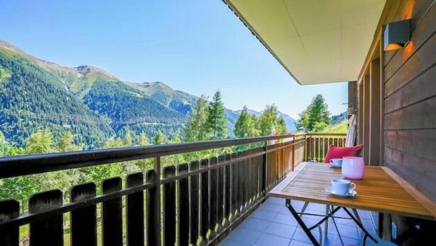 A balcony with a table and chairs, overlooking a mountainous landscape. - 4* renovated apartment at the top of the mountain at 1500 m (Goms)