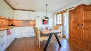 A kitchen with white cabinets, a wooden dining table, and a large wooden cabinet. - 4* renovated apartment at the top of the mountain at 1500 m (Goms)