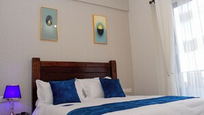 A neatly made bed with blue and white bedding, a wooden headboard, and two framed artworks on the wall. - Clean, cozy and welcoming space for all my guests. (Nairobi)