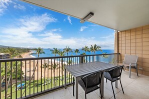 A balcony with a table and chairs, overlooking a beach and ocean. - Spectacular Ocean Views & Updated Interior at Mana Kai Maui Resort #706C (Kihei, Maui)