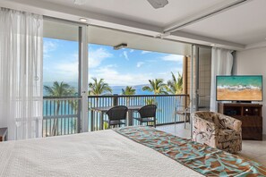A bedroom with a large bed, a TV, and a balcony with a view of the ocean. - Spectacular Ocean Views & Updated Interior at Mana Kai Maui Resort #706C (Kihei, Maui)