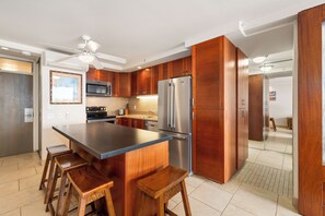 A modern kitchen with a central island, wooden cabinets, stainless steel appliances, and a ceiling fan. - Spectacular Ocean Views & Updated Interior at Mana Kai Maui Resort #706C (Kihei, Maui)