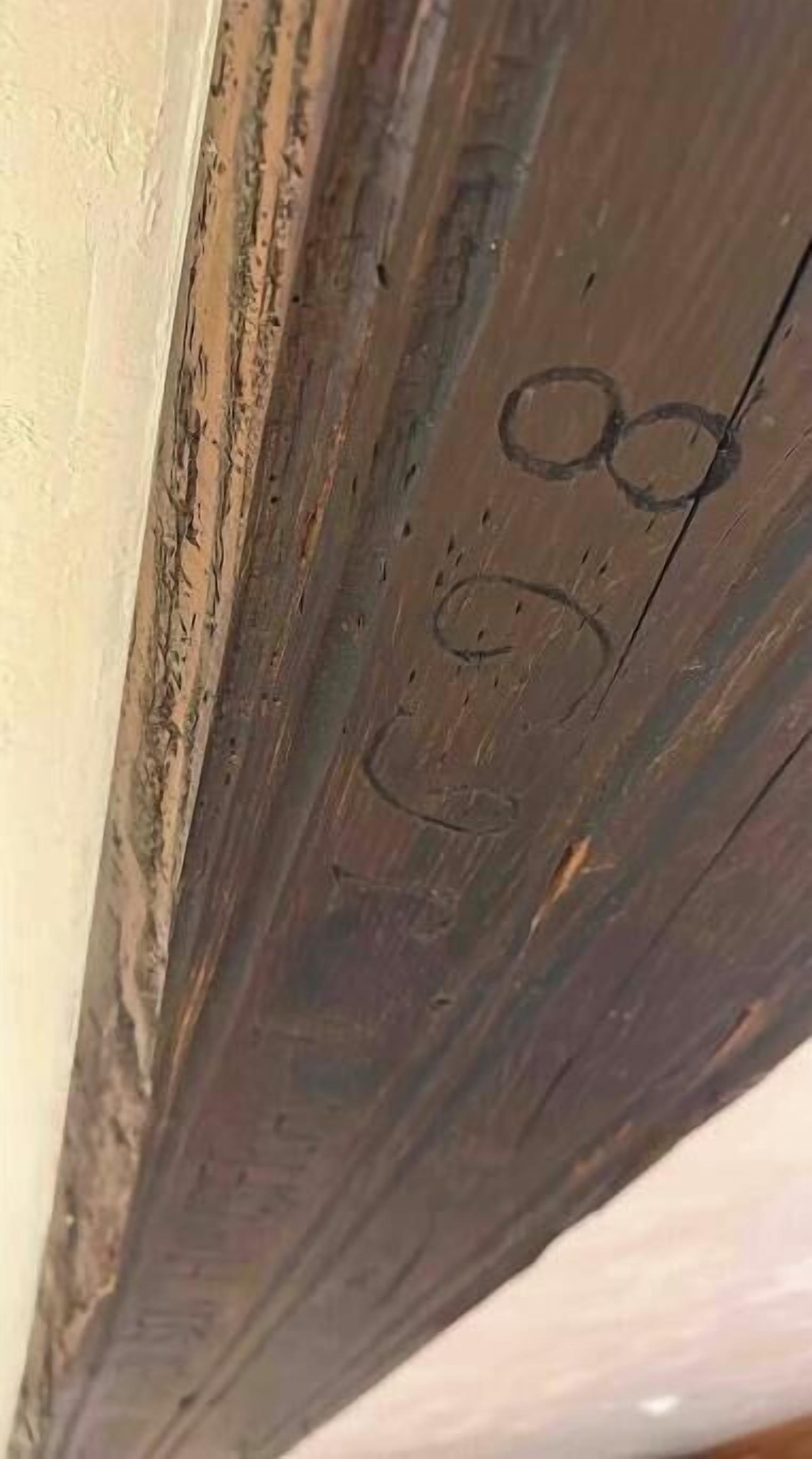Ein Nahblick auf einen Holzbalken mit Gebrauchsspuren und Beschriftungen.