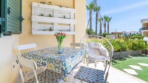A patio with a table and chairs, a hanging chair, a white planter with plants, and a white wall-mounted shelf with plants. - Apartment 'La Casa Di Chloe' with Wi-Fi and Air Conditioning (Pachino)