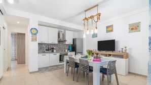 A modern kitchen with white cabinets, a dining table with chairs, a TV, and decorative wall art. - Apartment 'La Casa Di Chloe' with Wi-Fi and Air Conditioning (Pachino)