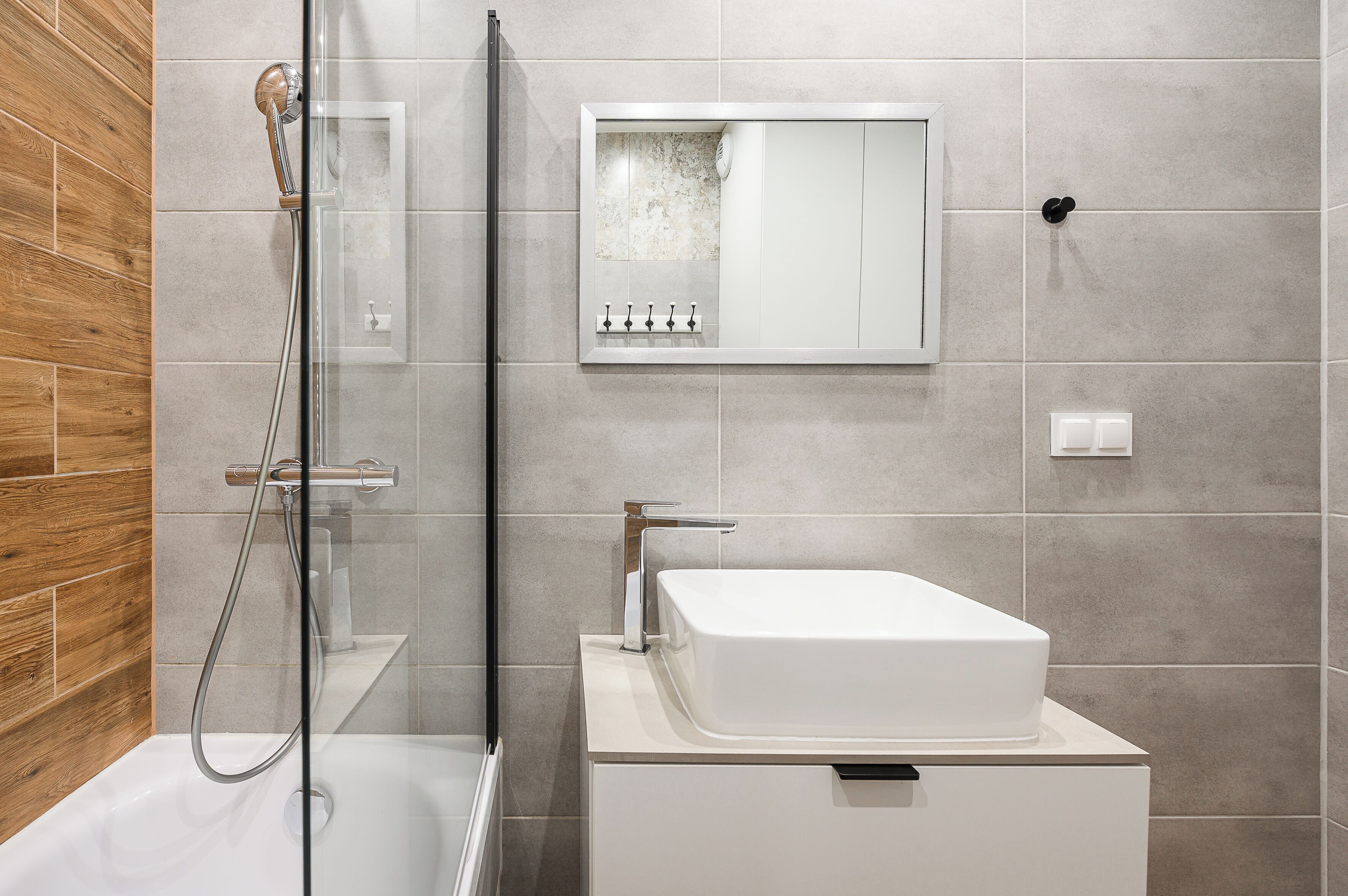 Un baño moderno con cabina de ducha de vidrio, un lavabo blanco y una pared de acento de madera.