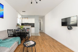 A modern living room with a sofa, dining table, chairs, and a TV mounted on the wall. - ShortStayPoland Daniszewska B192 (Warszawa)
