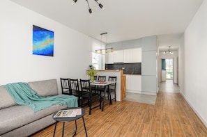 A modern living room with a sofa, dining table, and chairs, a kitchen area with cabinets and a countertop, and a hallway leading to another room. - ShortStayPoland Daniszewska B192 (Warszawa)