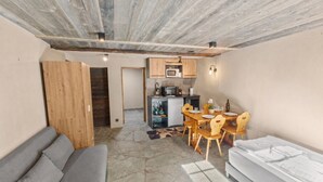 A compact living space with a stone floor, wooden furniture, a kitchenette, and a sofa. - Cozy studio in the heart of an Alpine chalet (Anniviers)