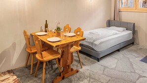 A room with a bed, a table set for two, and a window with curtains. - Cozy studio in the heart of an Alpine chalet (Anniviers)
