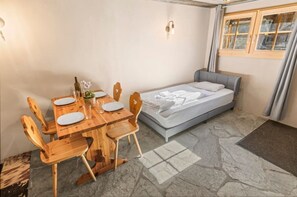 A small room with a bed, a wooden dining table with chairs, and a window. - Lovely studio in the basement of an authentic chalet (Anniviers)
