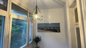Käytävällä on geometrisen muotoinen riippuvalaisin, seinälle ripustettu taulu ja ruukussa oleva kasvi.
