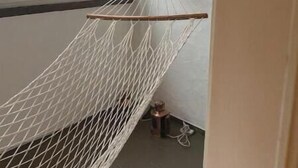 Eine Hängematte in einem Zimmer mit Fenster, ein Gemälde an der Wand und ein kleiner Tisch mit Lampe.