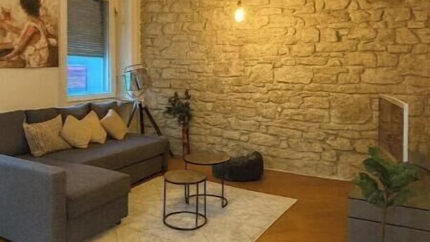 Ein Wohnzimmer mit Steinswand, grauem Sofa, kleinem runden Tisch und einer Pendelleuchte.