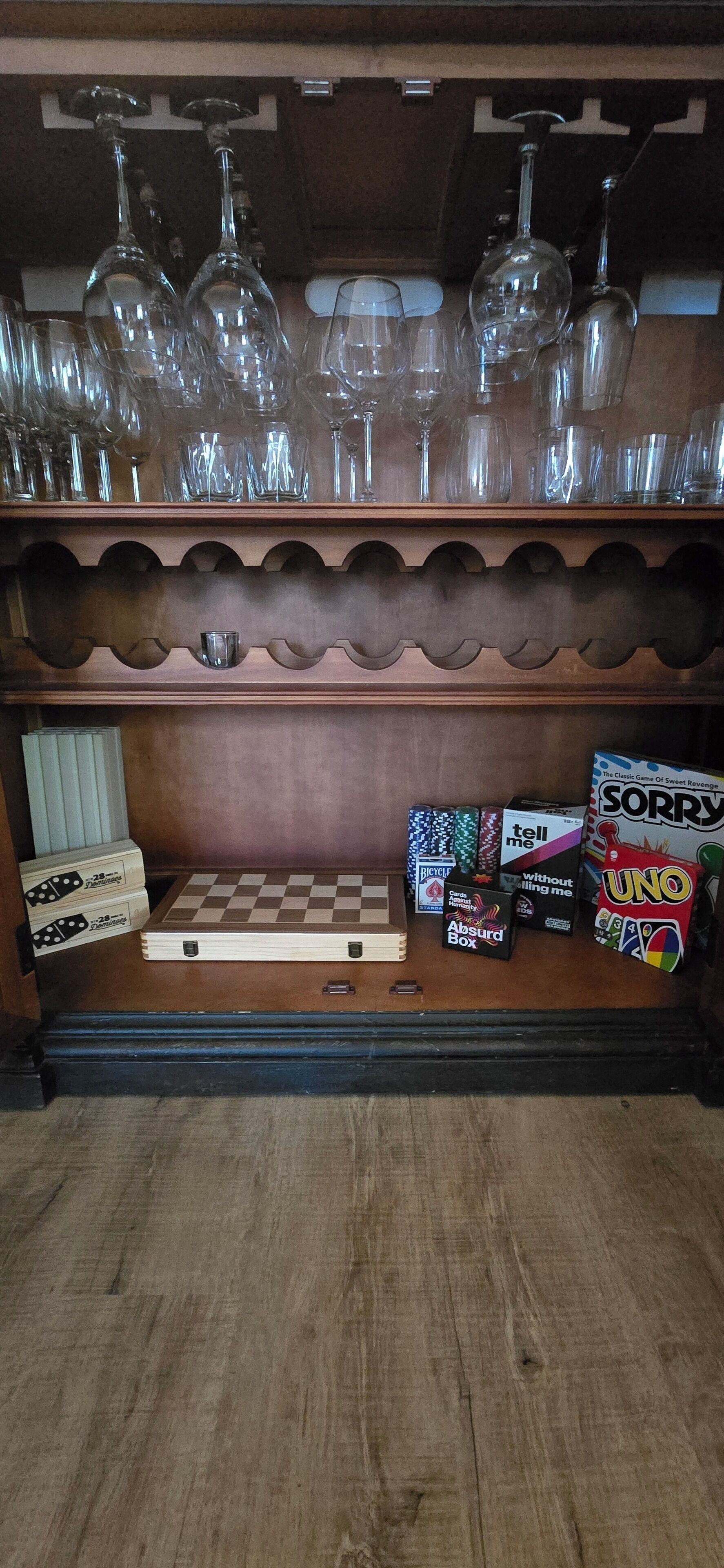 A wooden shelf with wine glasses, a chessboard, and various board games.