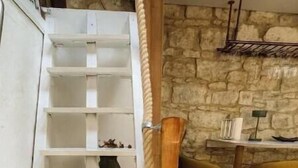 A white wooden ladder leading to a lofted area with a stone wall and a small table with chairs.