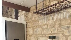 A kitchen with a stone wall, a stainless steel refrigerator, a white countertop, and two yellow chairs.