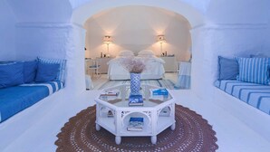 A room with a bed, a white coffee table with books, a desk, and two lamps. - Private Andalusian Estate for Groups Retreats (Cazalla De La Sierra)