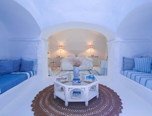 A room with a bed, a white coffee table with books, a desk, and two lamps.