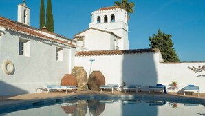 A pool with clear water reflecting the surrounding buildings, a white building with a bell tower, and a clear blue sky. - Private Andalusian Estate for Groups Retreats (Cazalla De La Sierra)