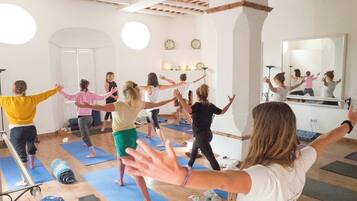 A yoga class in a room with wooden beams, a large mirror, and a white wall with shelves.
